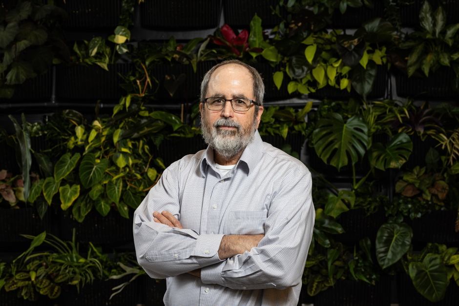 Ron Mittler posing in front of a wall of plants at Mizzou.